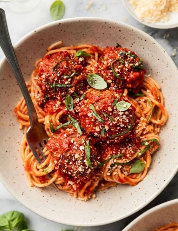 Baked Italian meatballs coated in red sauce over spaghetti noodles in a bowl