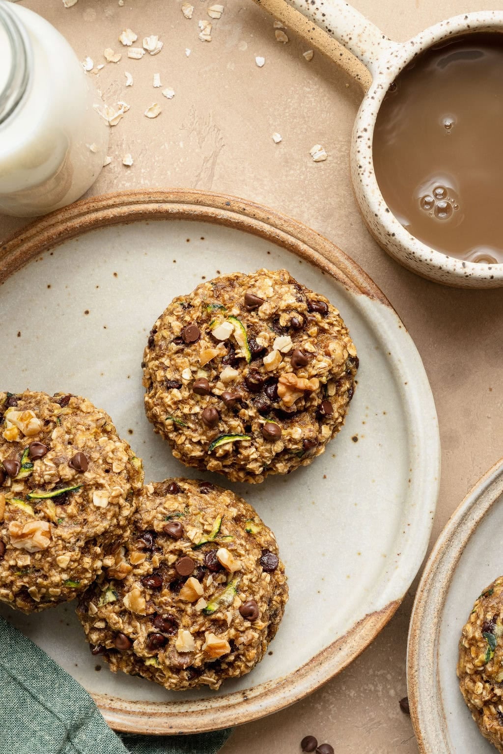 Three zucchini cookies on a plate next to a mug of coffee.