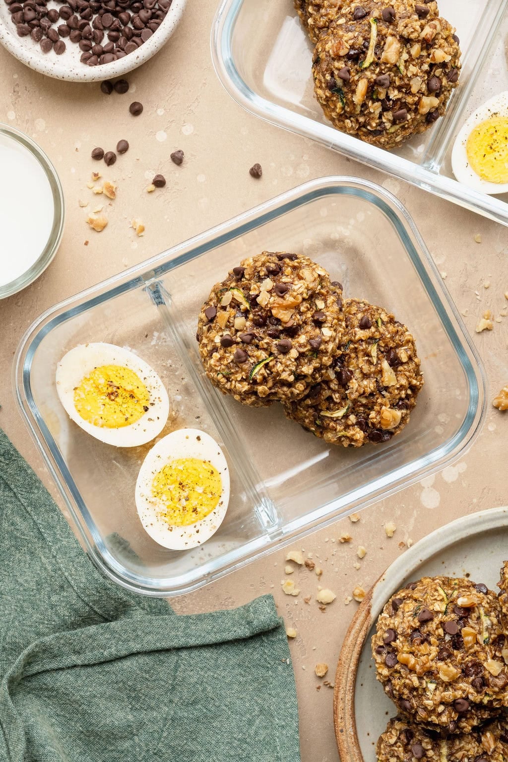 Two glass meal prep containers, each filled with two zucchini cookies and two hard-boiled egg halves.