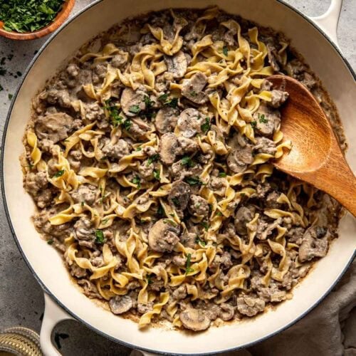 Overhead view of a cast iron pan filled with ground beef stroganoff topped with fresh herbs.