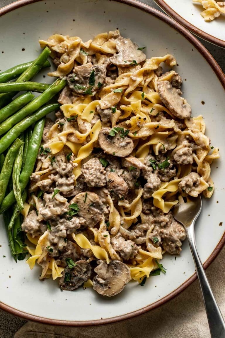 Overhead view of Easy and Delicious Ground Beef Stroganoff on a plate with green beans on the side.