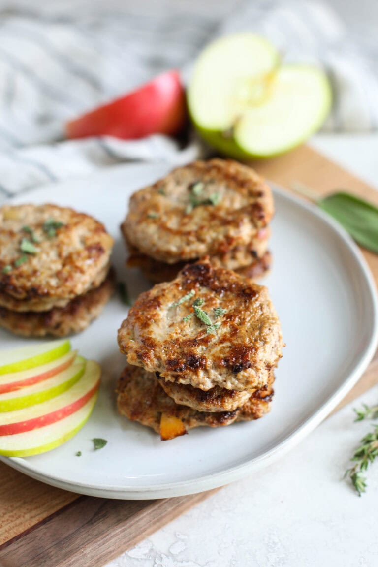 Close up view of a plate of small stacks of turkey apple sausage patties topped with fresh sage. 