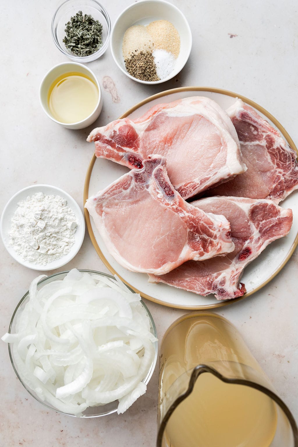 Overhead view of a variety of ingredients for The Best Smothered Pork Chops in different sized bowls and plates. 