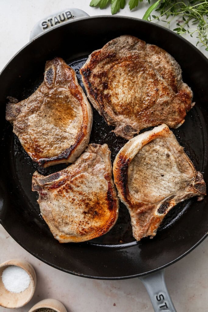 Overhead view of a cast iron skillet with freshly browned bone-in pork chops. 