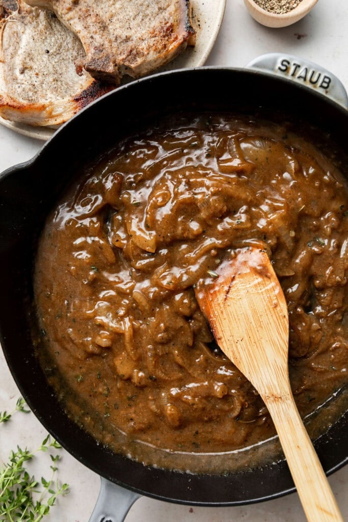 Overhead view of a cast iron skillet filled with brown gravy mixture for The Best Smothered Pork Chops. 