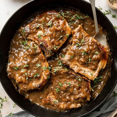 Pork chops coated in gravy in a cast iron skillet