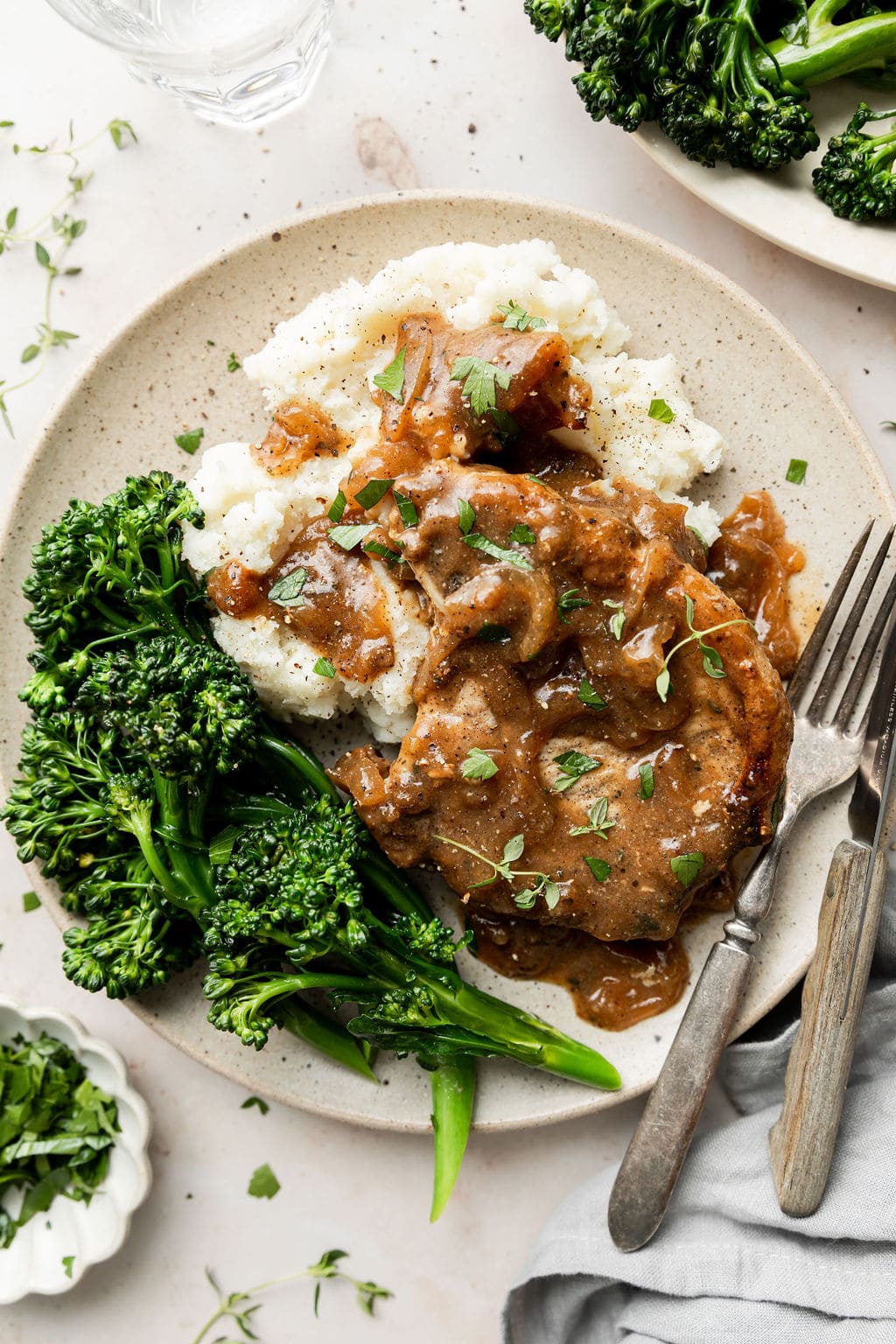 Overhead view of a plate of The Best Smothered Pork Chops with mashed potatoes and freshly steamed broccoli. 