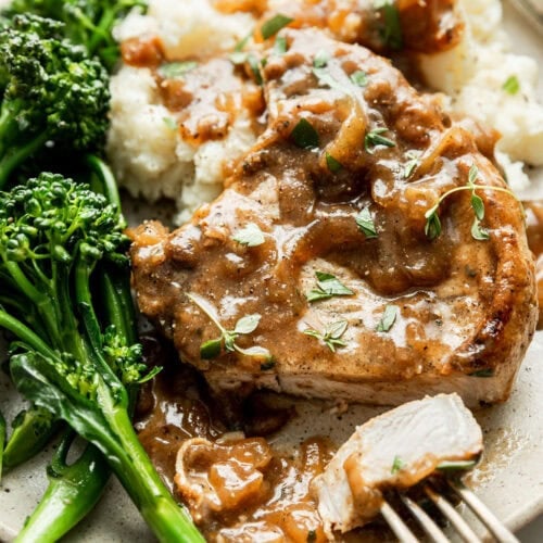 Overhead view of a plate of smothered pork chops over mashed potatoes and broccolini on the side.