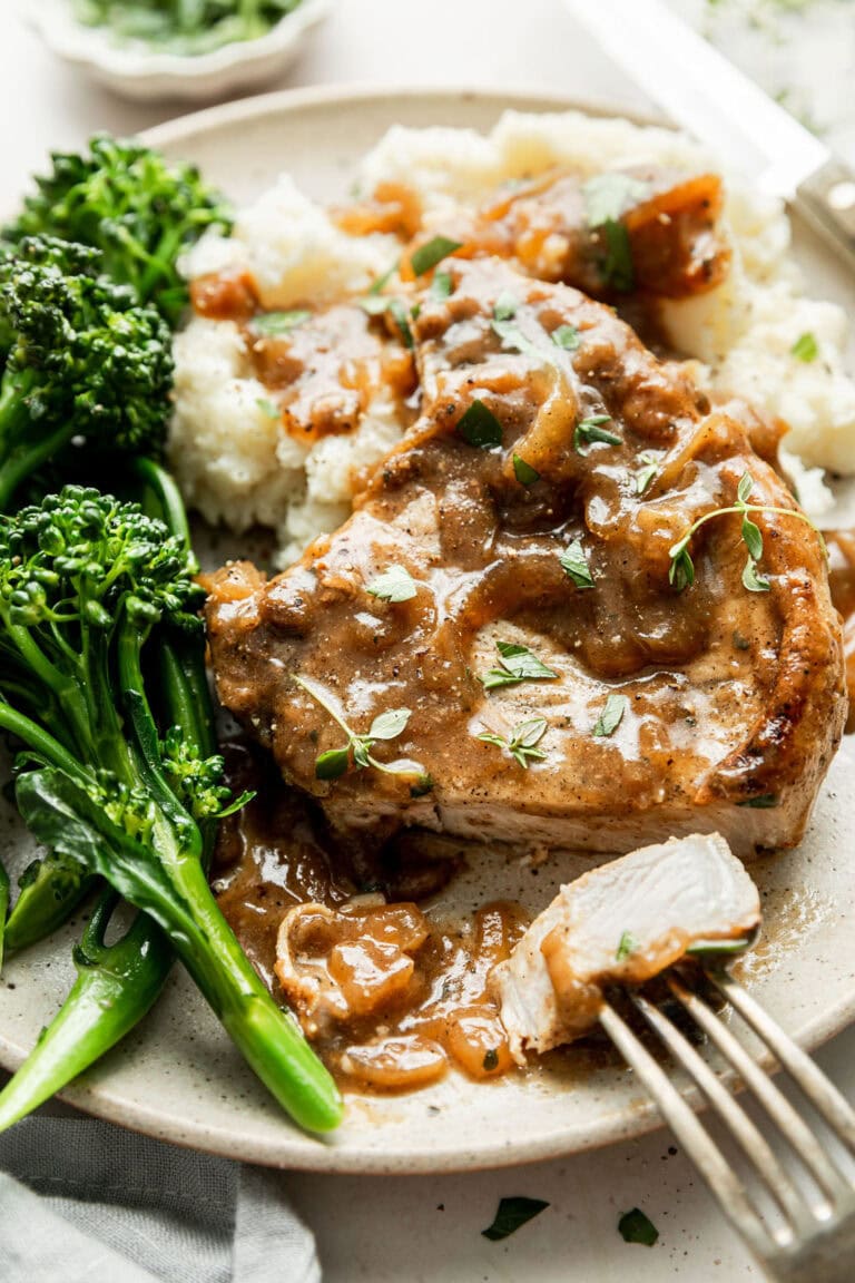 Overhead view of a plate of smothered pork chops over mashed potatoes and broccolini on the side.