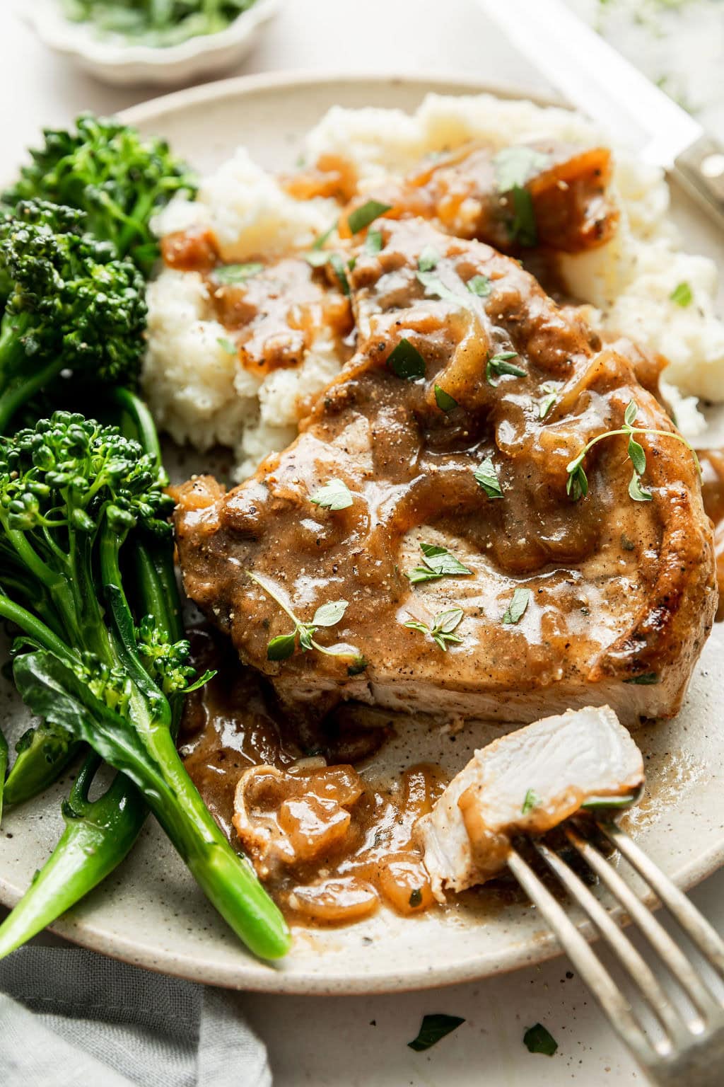 Close up view of a plate of The Best Smothered Pork Chops with mashed potatoes and steamed broccoli. 