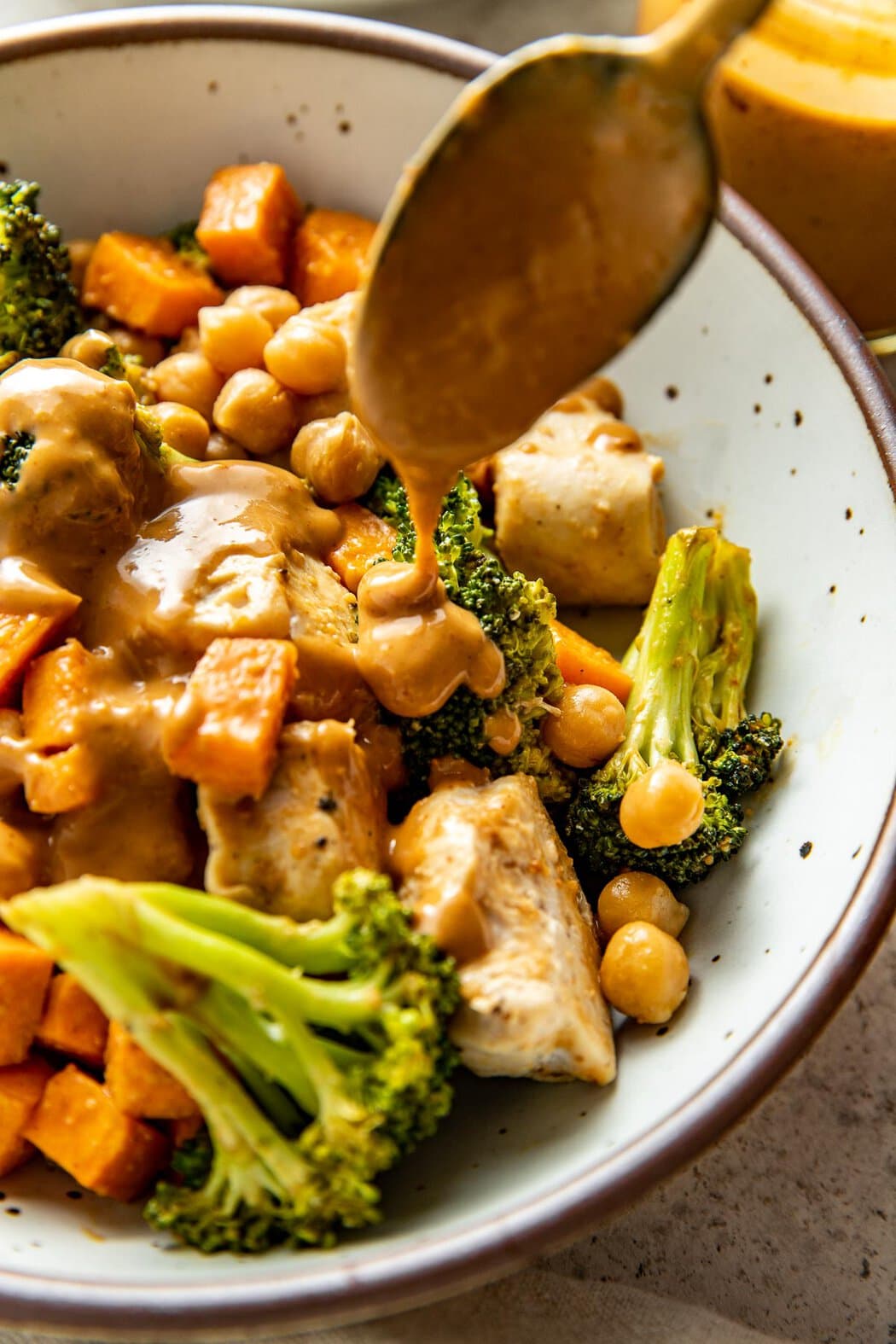 Close up view of a Thai-Inspired Sweet Potato Peanut Bowl with Chicken being drizzled with peanut sauce. 