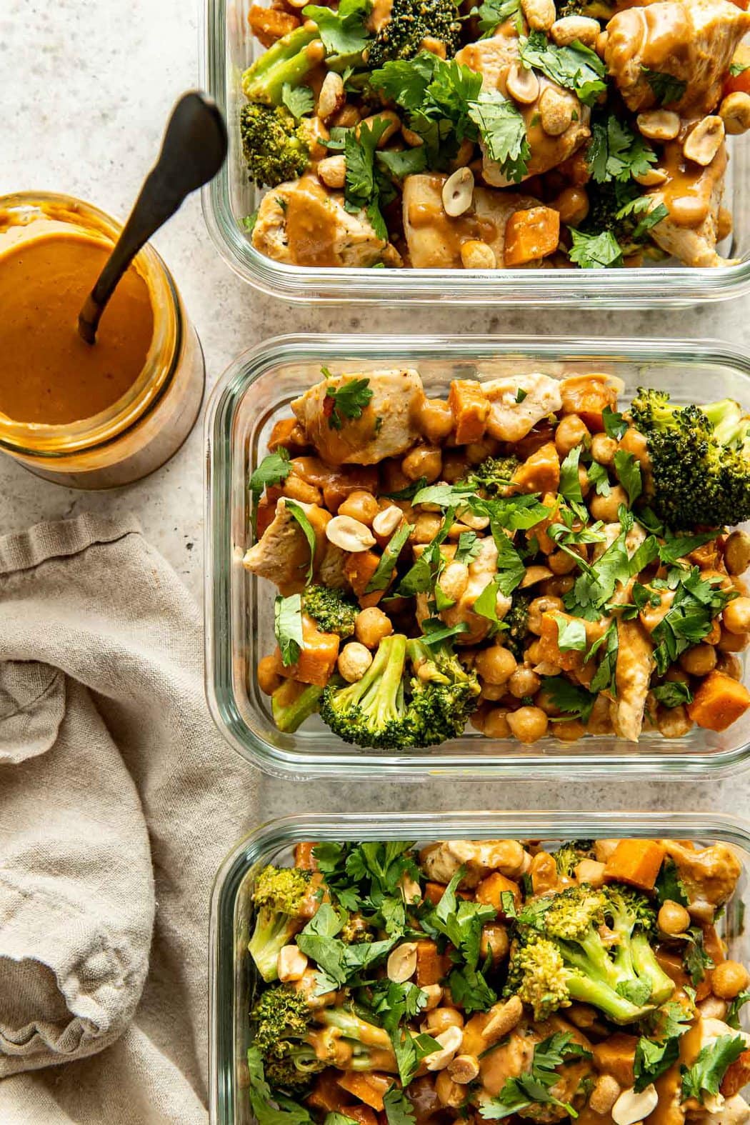 Overhead view of three glass meal prep containers filled with Thai-Inspired Sweet Potato Peanut Bowl with Chicken and topped with fresh cilantro.