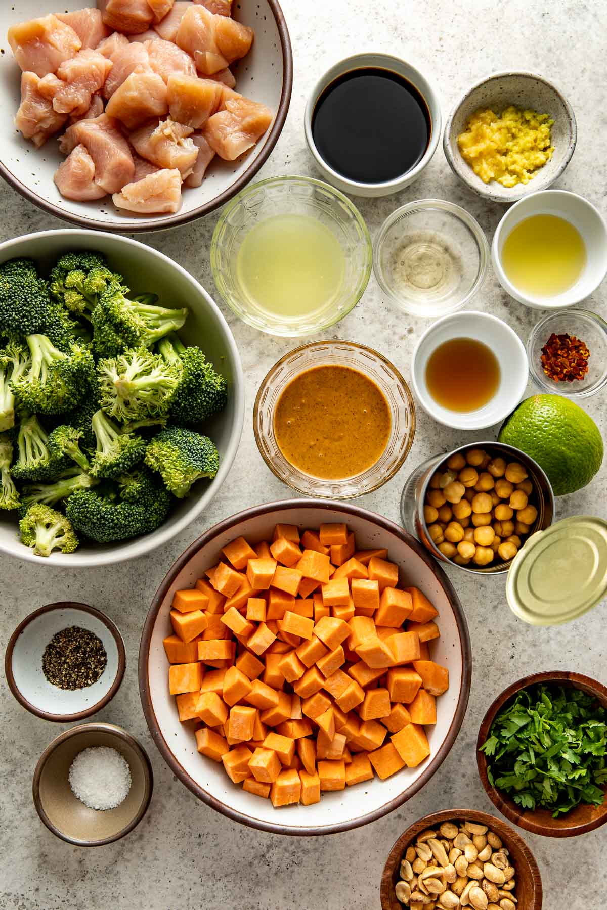 Overhead view of a variety of ingredients for Thai-Inspired Sweet Potato Peanut Bowl with Chicken in different sized bowls. 