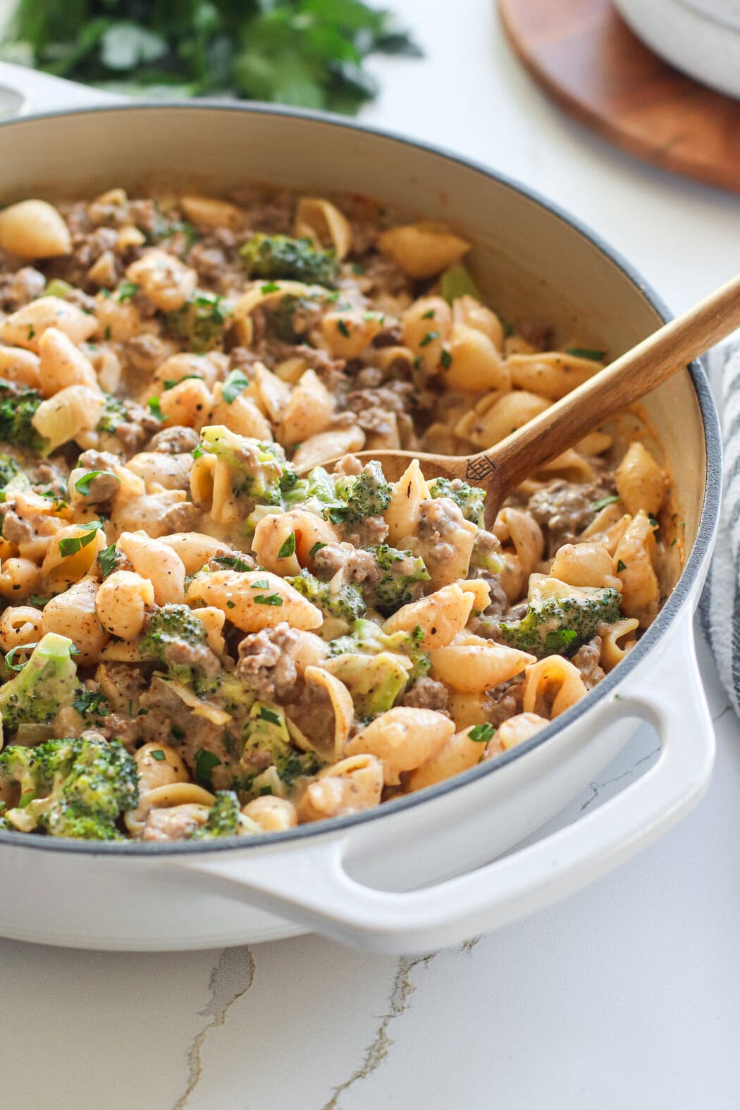 A wooden spoon stirring Homemade Hamburger Helper ingredients in a white skillet. 