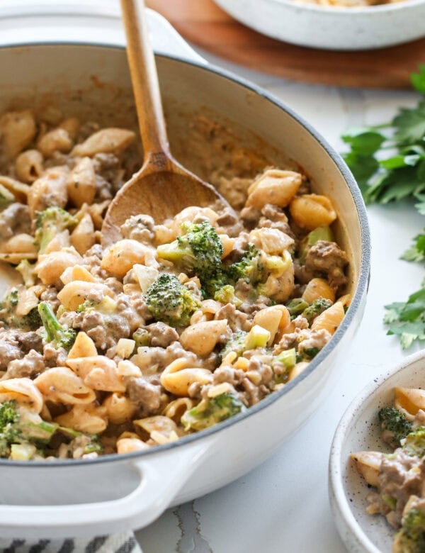 Homemade hamburger helper with broccoli in white skillet with wooden serving spoon