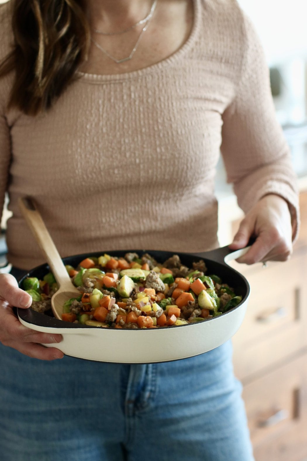 A woman holding a cast iron skillet filled with a brussels sprouts hash. 