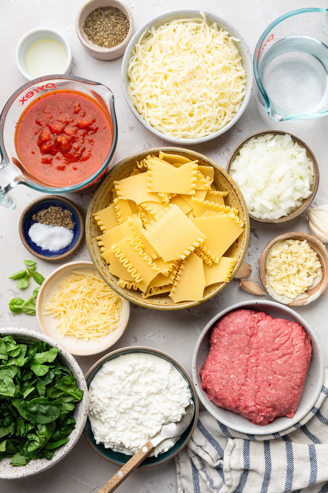 Overhead view of a variety of ingredients for Crockpot Lasagna in different sized bowls. 