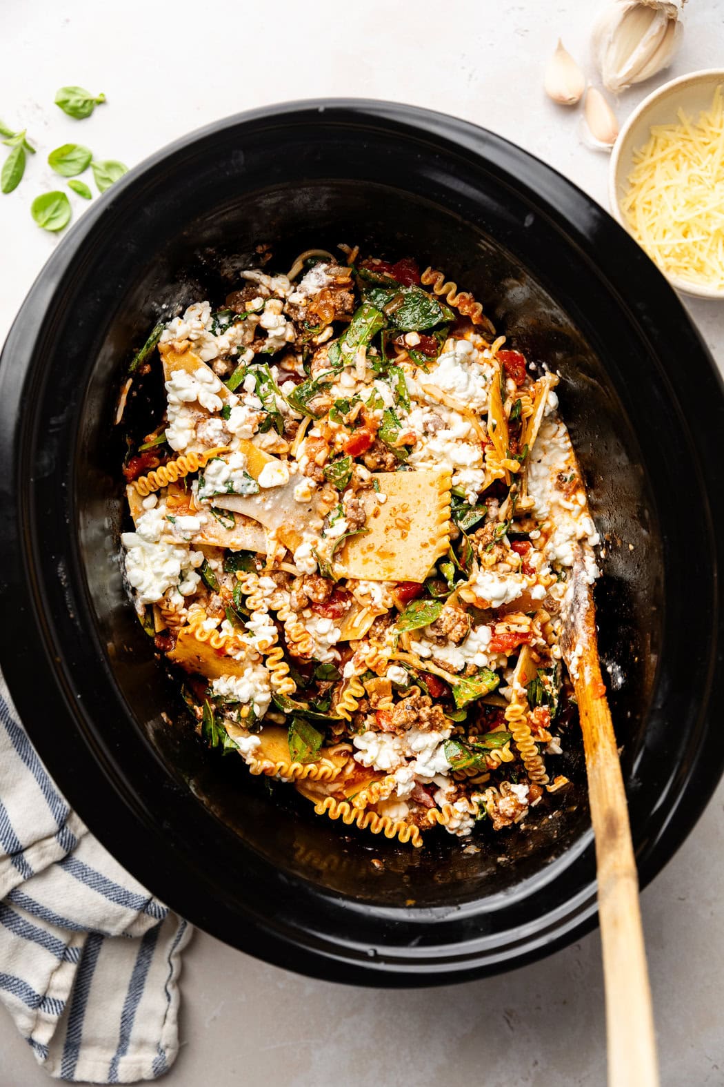 Overhead view of a slow cooker with ingredients for Crockpot Lasagna being stirred with a wooden spoon. 