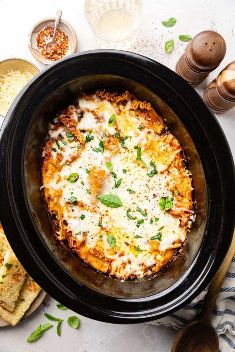 Overhead view of a Crockpot filled with cheesy Lasagna topped with fresh basil. 