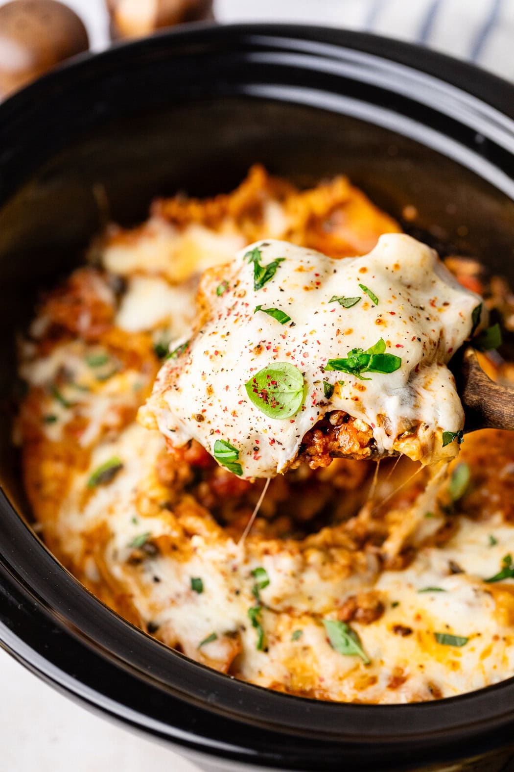 Close up view of a wooden spoon scooping a large spoonful of Crockpot Lasagna. 