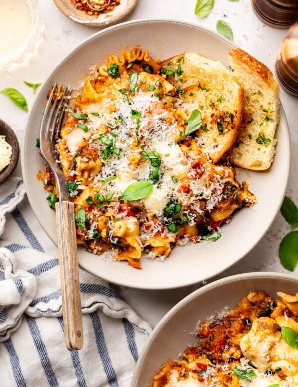 Crockpot lasagna serving on white plate with garlic bread on the side