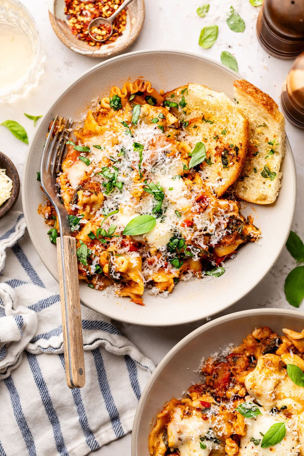 Overhead view of a white plate of Crockpot Lasagna topped with parmesan cheese and fresh basil. 