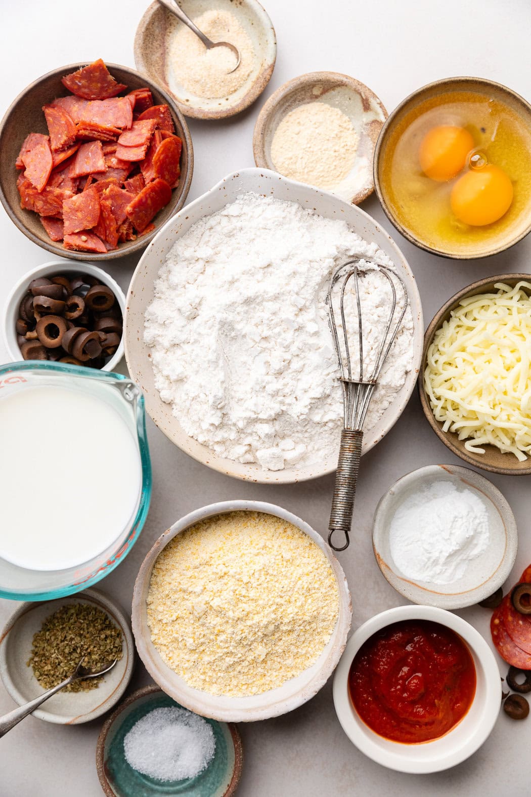 Overhead view of a variety of ingredients for Pepperoni Pizza Muffins in different sized bowls. 