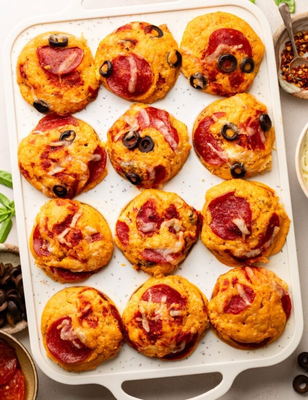 Overhead view pizza muffins in muffin pan, topped with black olives, melted cheese and pepperonis
