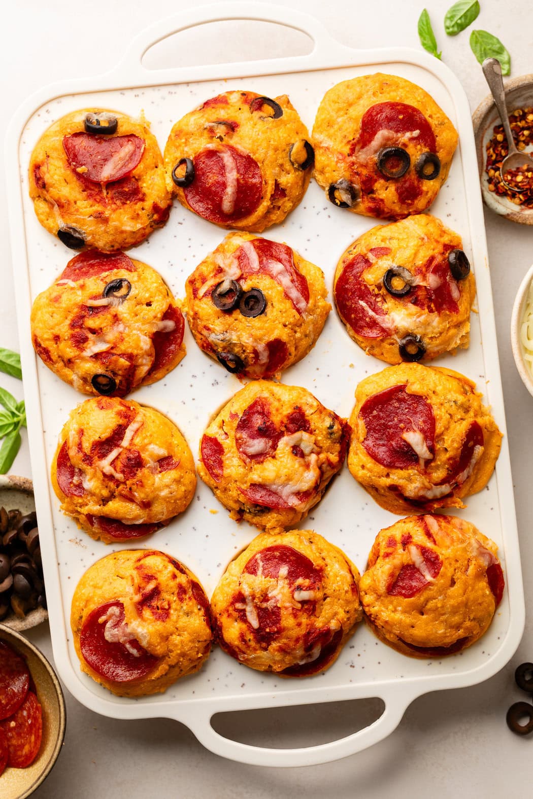 Overhead view of a freshly baked pan of Pepperoni Pizza Muffins topped with melted cheese and black olives. 