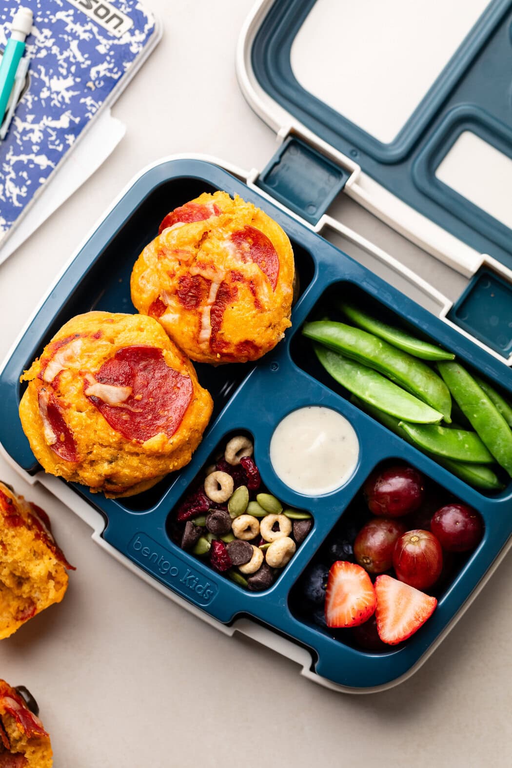 A bento lunch box filled with Pepperoni Pizza Muffins, fruit, veggies, and trail mix. 