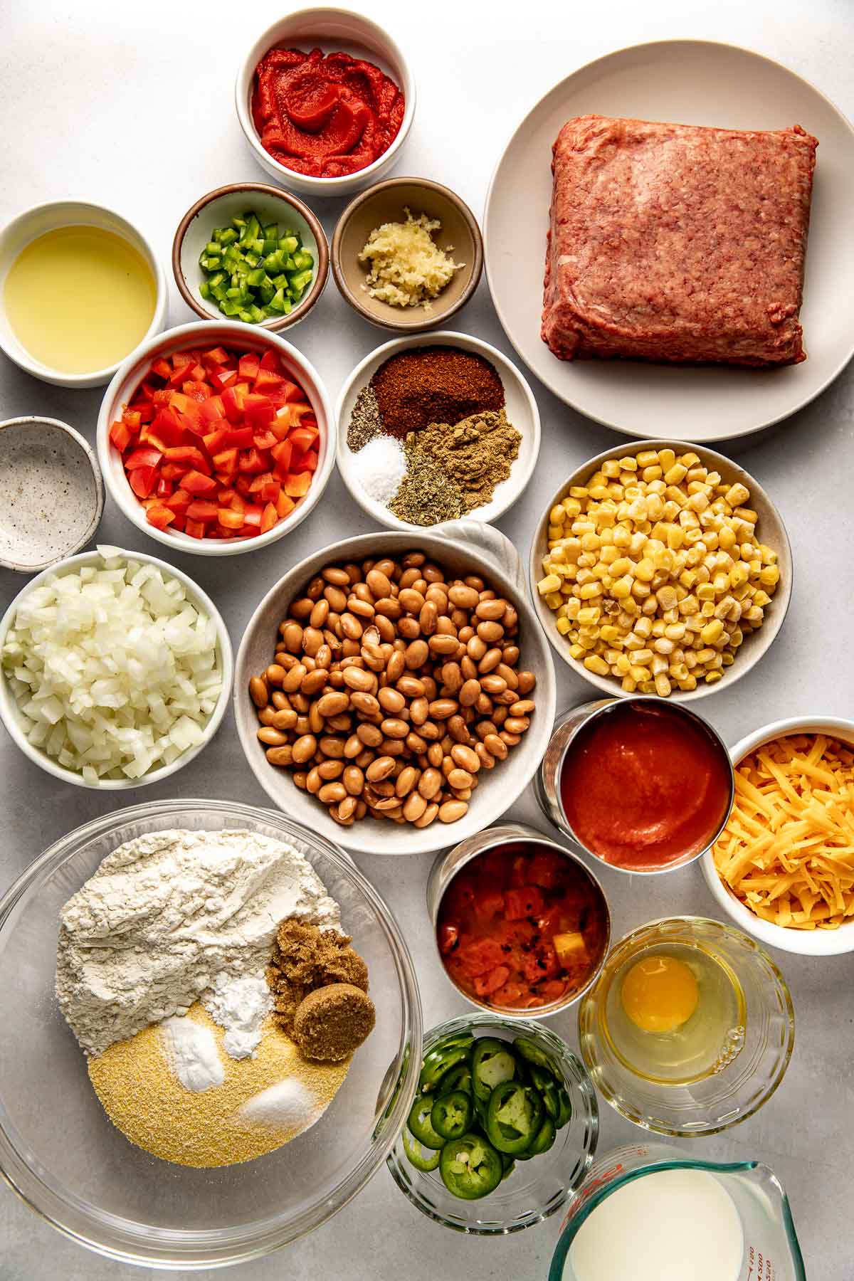 Overhead view of a variety of ingredients for Chili Cornbread Casserole in different sized bowls. 