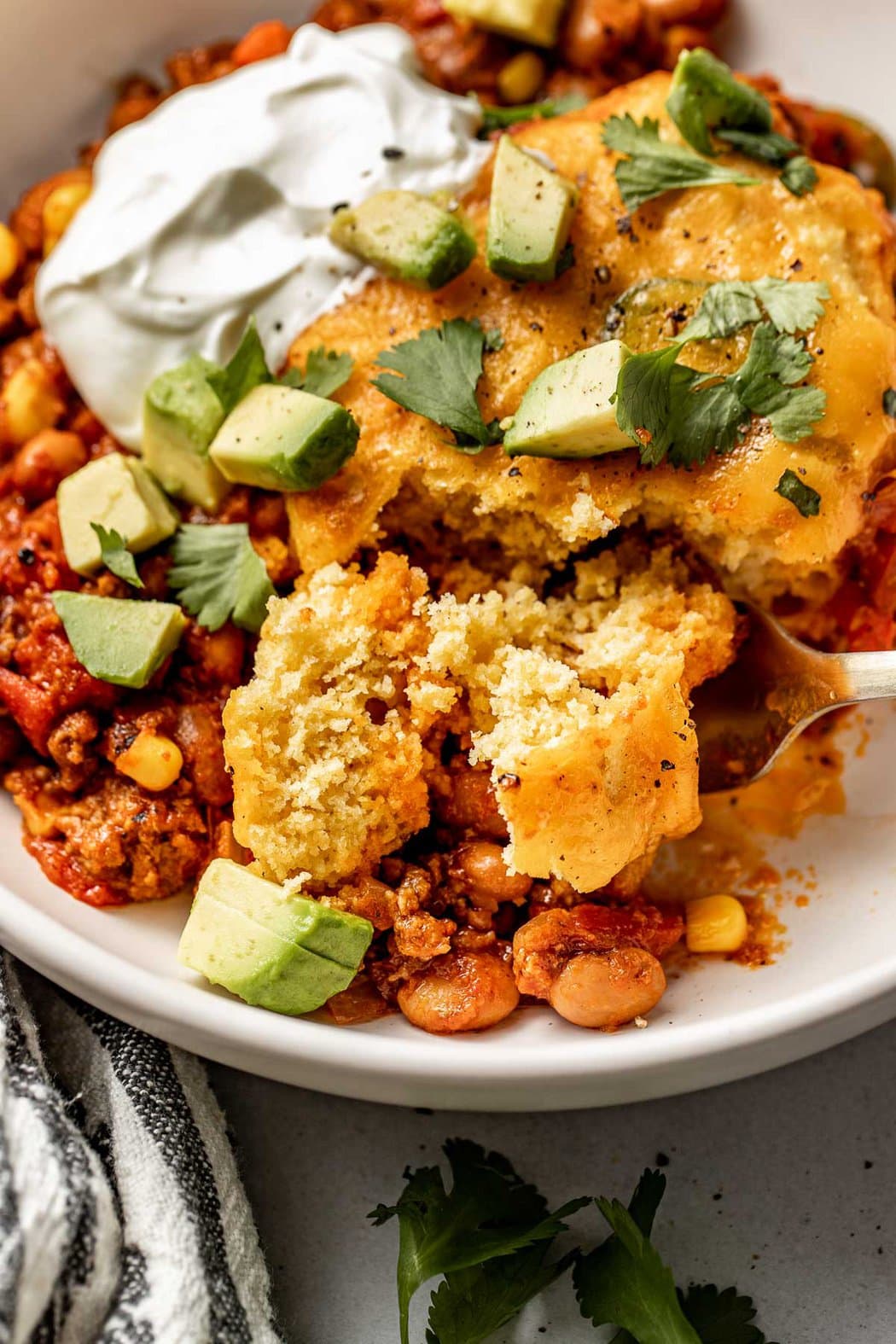 Close up view of a plate of Chili Cornbread Casserole topped with avocado, cilantro, and black pepper.