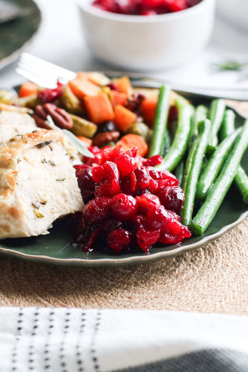 Close up view of a plate filled with traditional thanksgiving foods including roasted turkey, green beans and homemade cranberry sauce. 