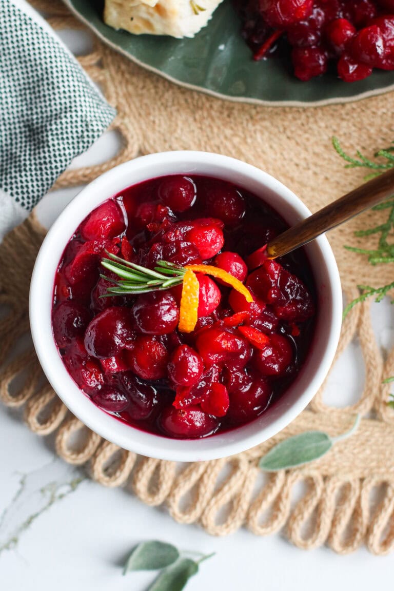Overhead view of a dish of homemade cranberry sauce topped with orange peel and thyme sprig. 