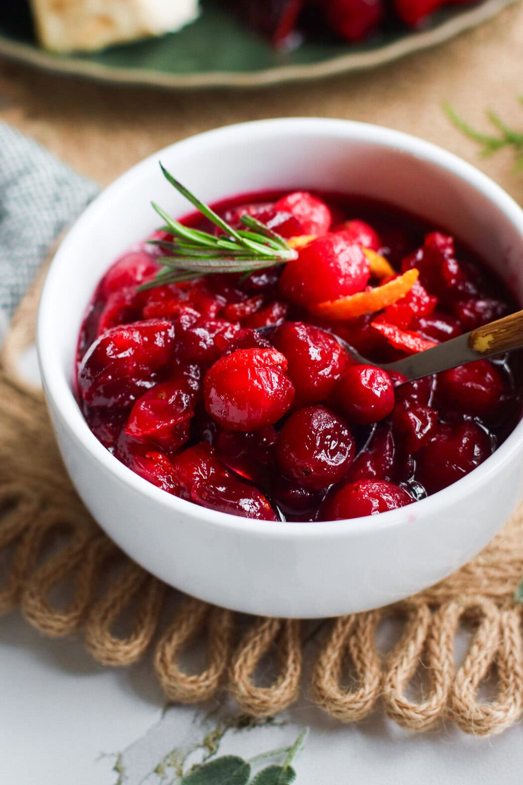 Close up view of a bowl of homemade cranberry sauce topped with orange zest and a fresh thyme sprig. 