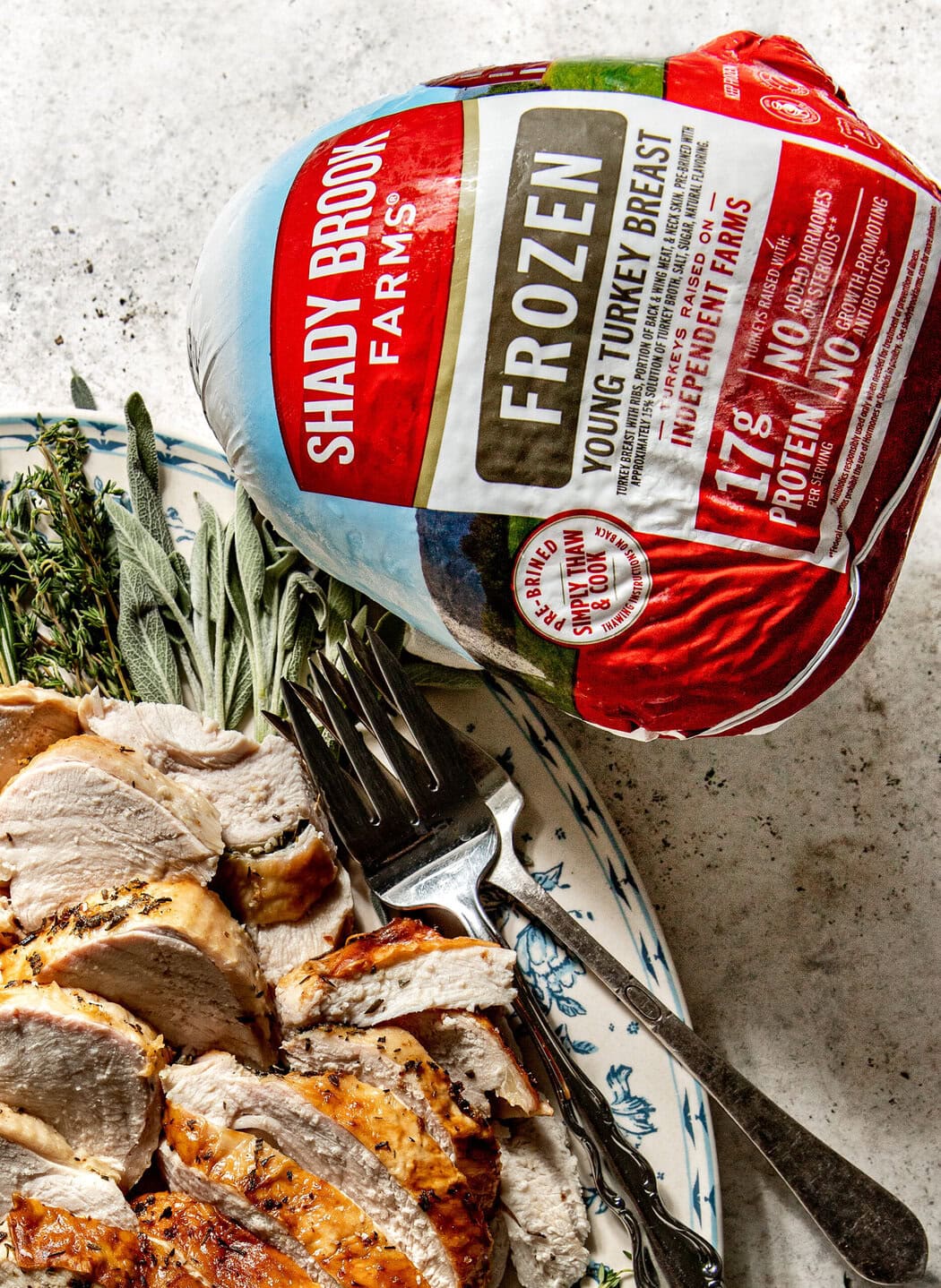 Overhead view of a plate of freshly roasted and sliced bone in turkey breast with a shady brook frozen turkey breast beside the plate.