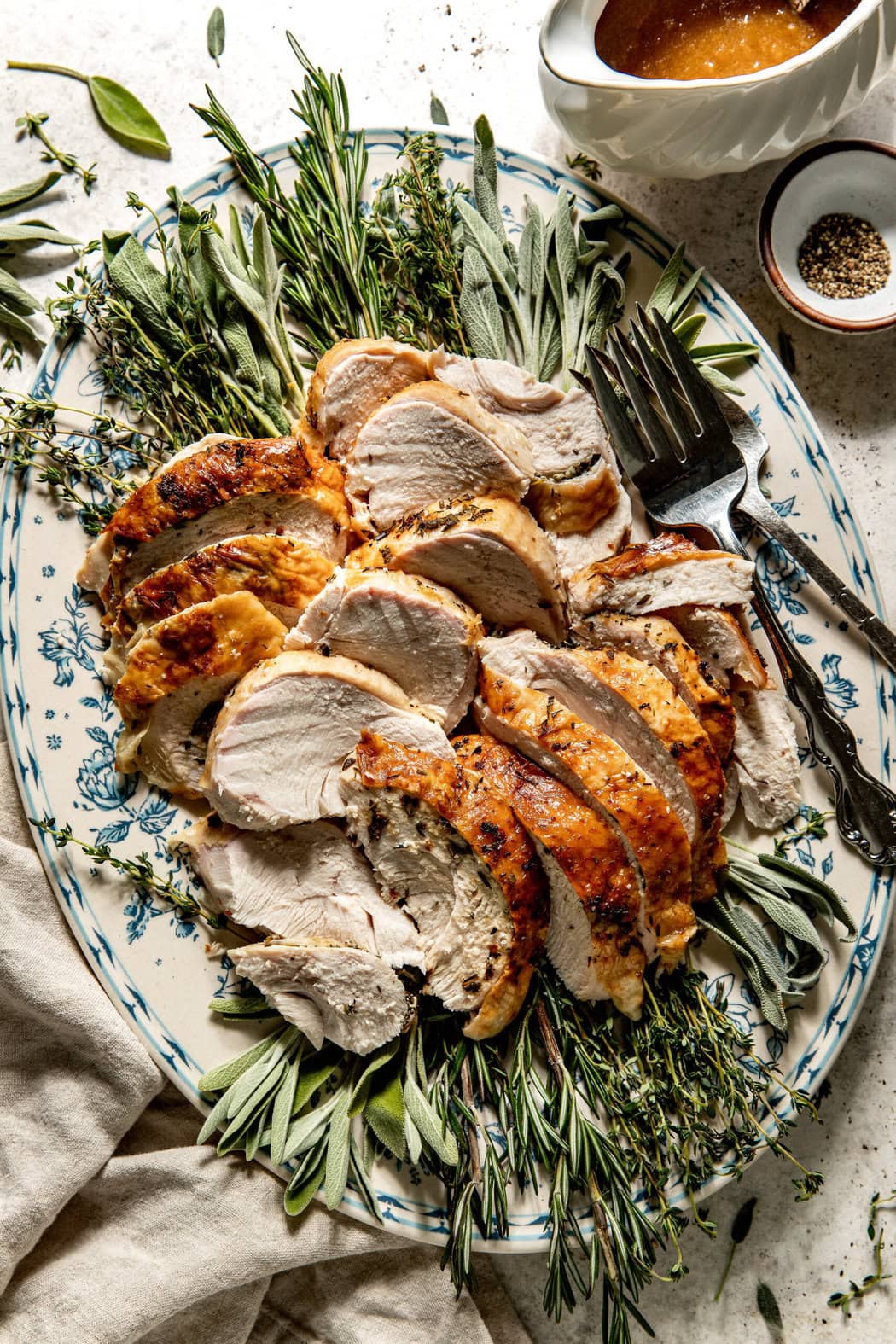 Close up view of a platter filled with sliced turkey breast surrounded by fresh herbs and spices. 