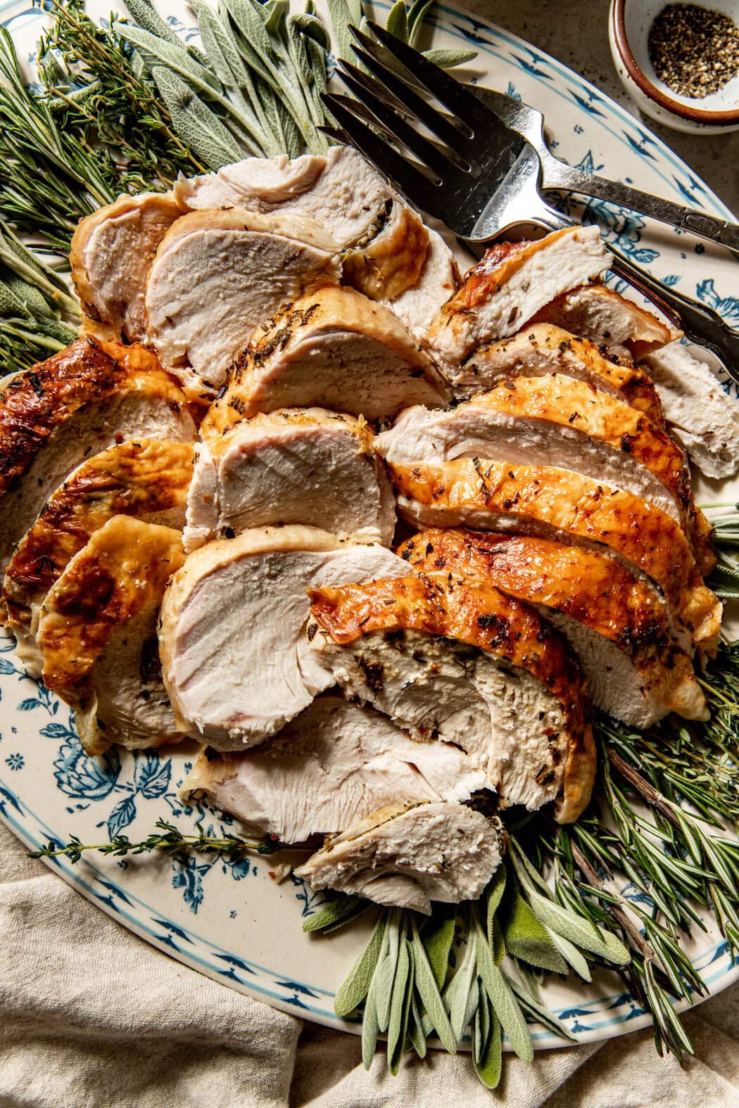 Overhead view of a plate of freshly roasted simple Bone-In Roasted Turkey Breast, sliced with fresh herbs surrounding it. 