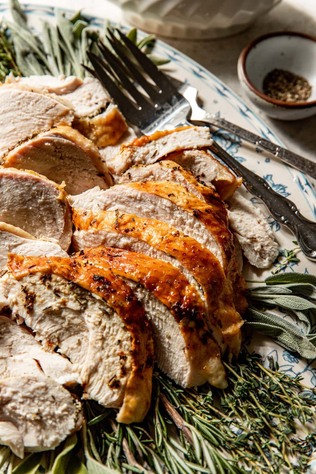 Close up view of a freshly roasted and sliced bone in turkey breast on a platter surrounded by fresh herbs. 