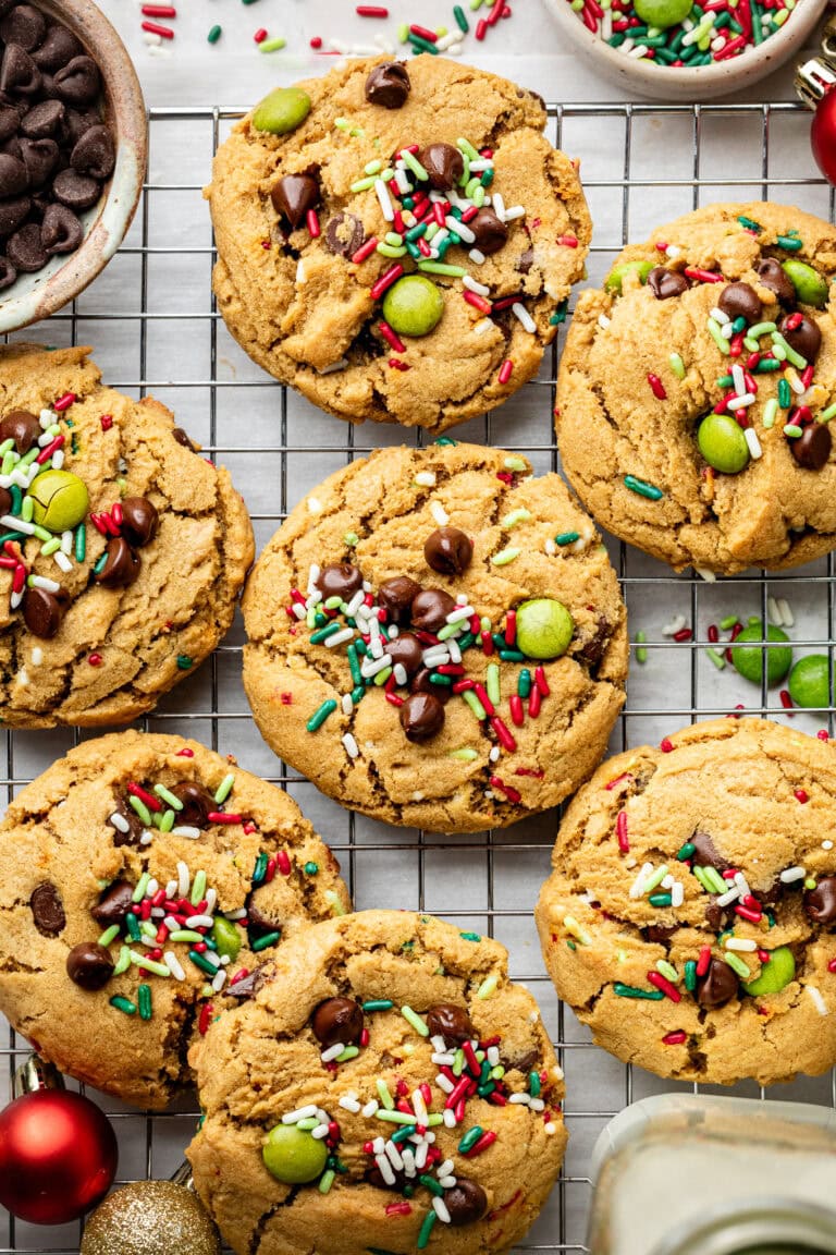 Overhead view of a cooling rack of festive Christmas cookies topped with sprinkles and chocolate pieces. 