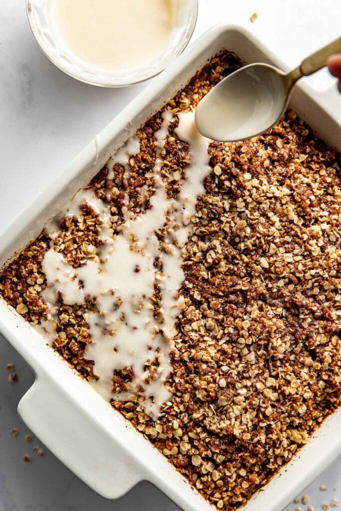 Overhead view of a pan of Cinnamon Streusel-Topped Baked Oatmeal being drizzled with a spoonful of icing. 