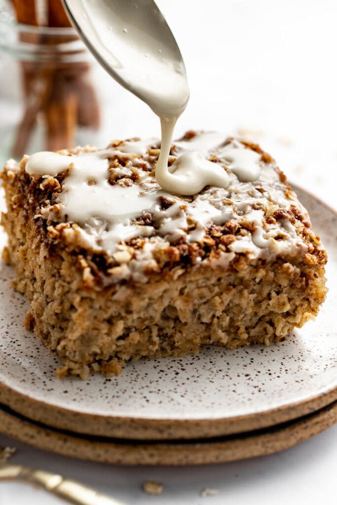 Close up view of a spoon drizzling icing on a piece of freshly baked Cinnamon Streusel-Topped Baked Oatmeal. 