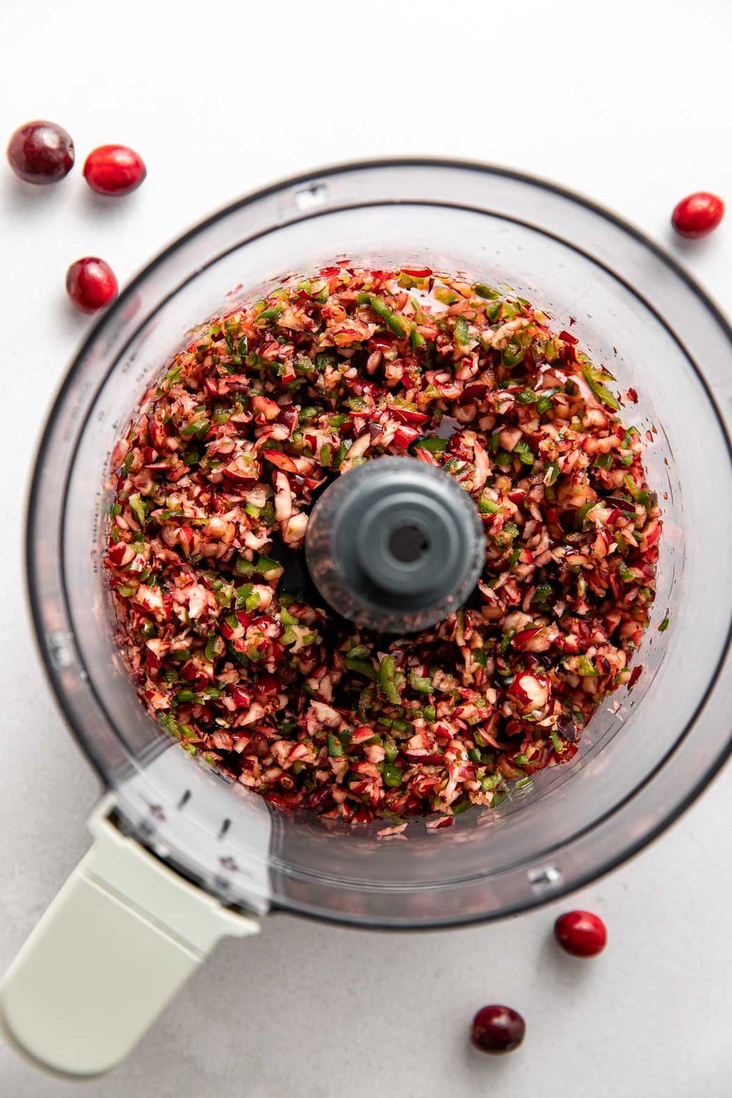 Overhead view of chopped cranberries and jalapenos in a food processor. 