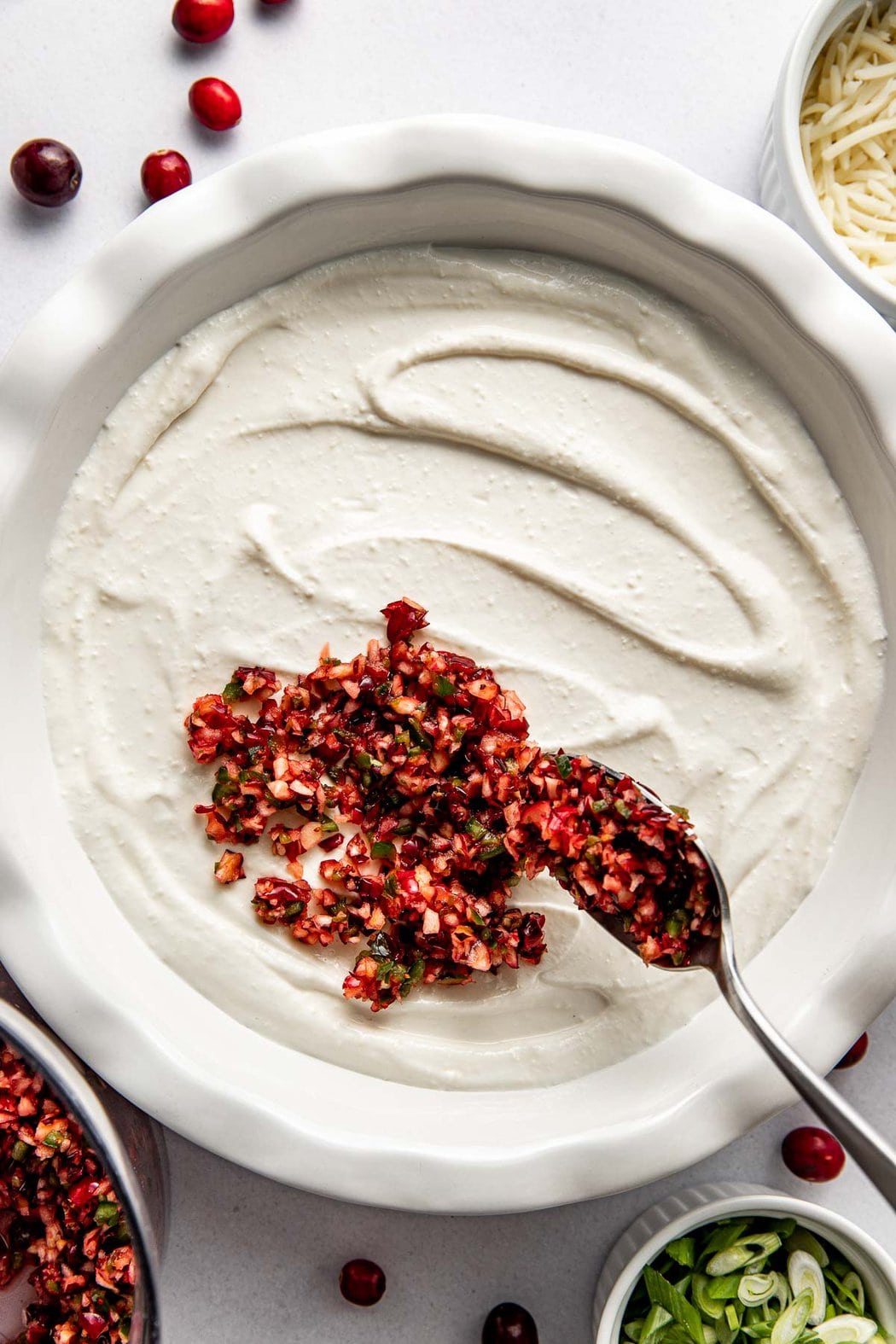 Overhead view of a dish filled with whipped cottage cheese being topped with a cranberry jalapeno mixture with a spoon. 