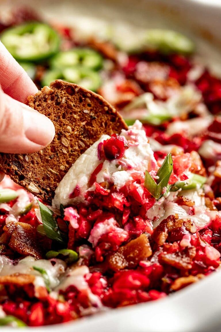 A thick cracker scooping up whipped cottage cheese dip with fresh cranberry pieces