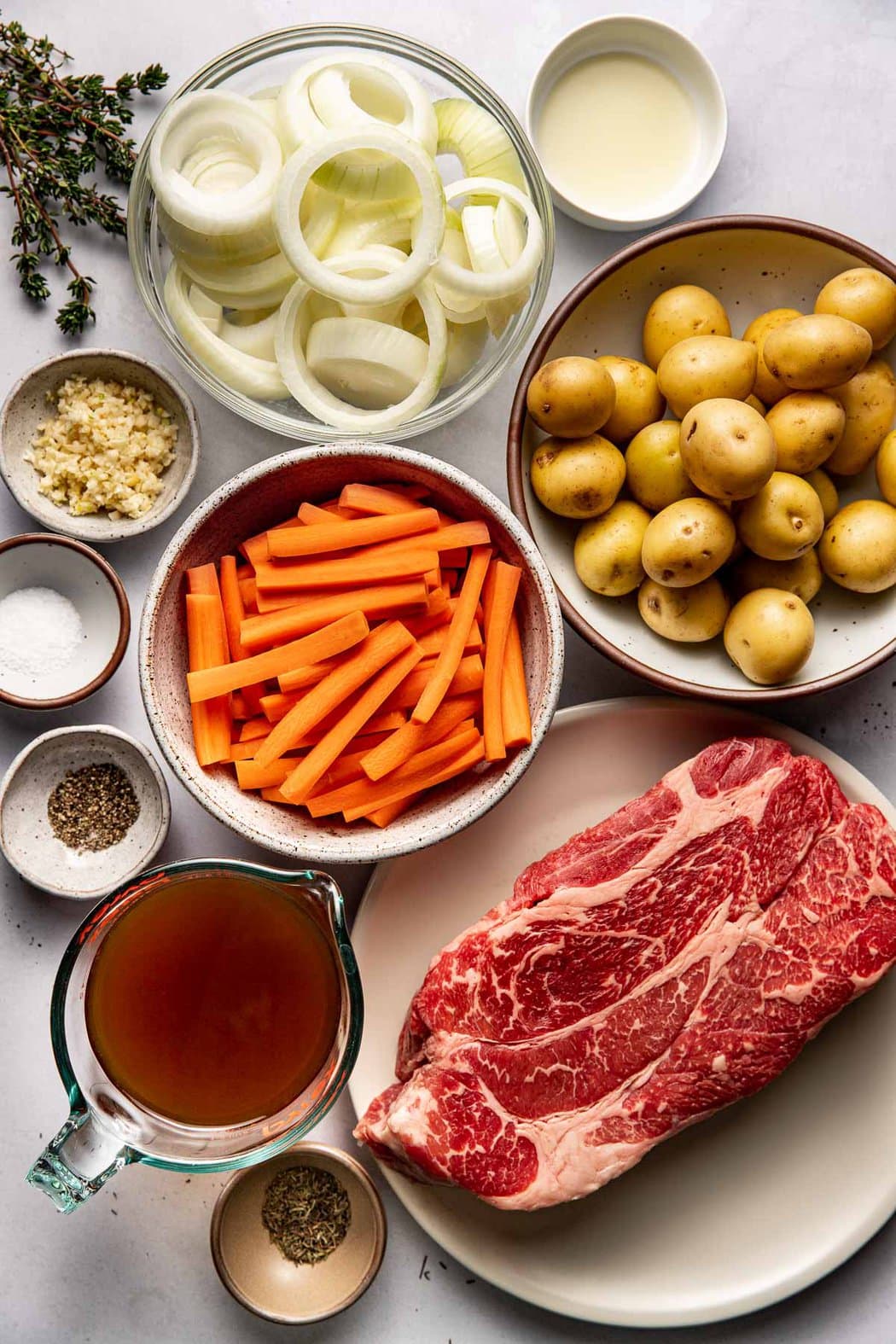 Overhead view of a variety of ingredients for Slow Cooker Pot Roast in different sized bowls. 