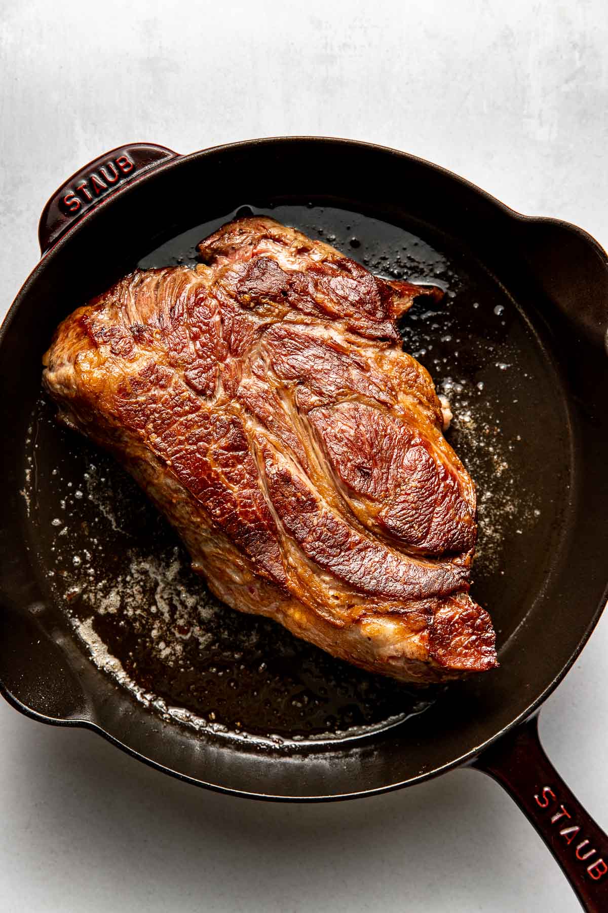 Overhead view of a freshly seared pot roast in a cast iron pan, ready for the slow cooker. 