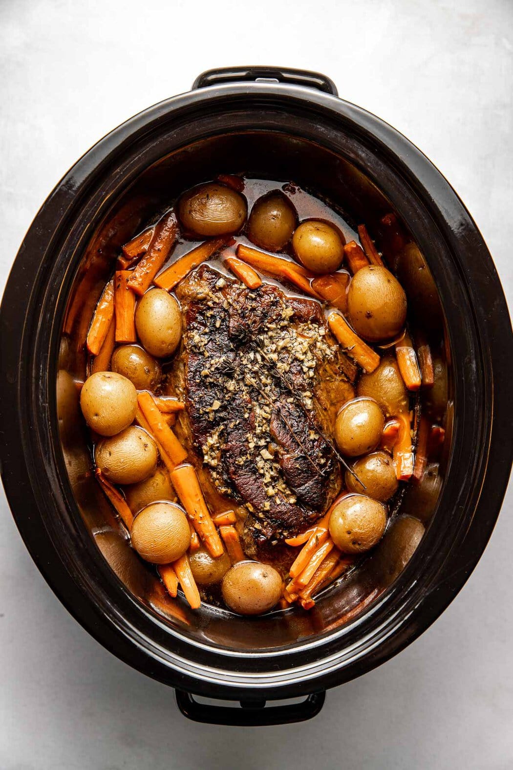 Overhead view of a slow cooker filled with Pot Roast, carrots, and potatoes. 