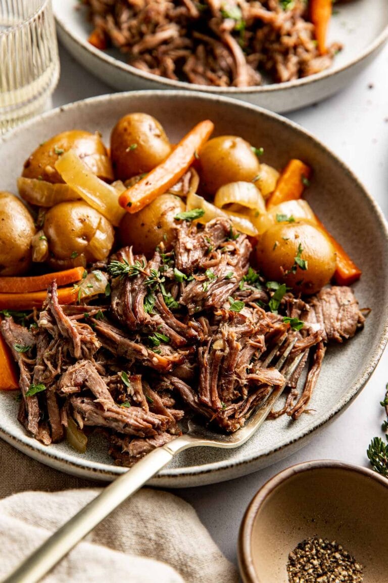 A shallow bowl filled with serving of pot roast with baby potatoes and carrots.
