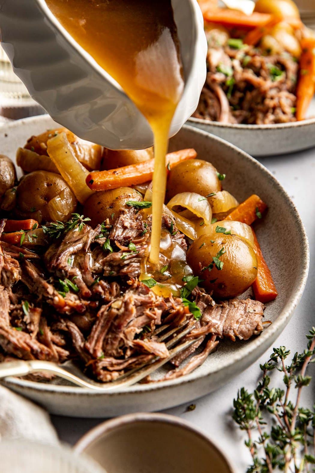 Close up view of a plate of Slow Cooker Pot Roast with gravy being poured on top. 